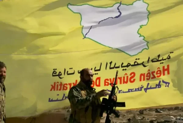 Due miliziani dell'SDF in posa davanti alla bandiera del gruppo.